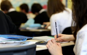 main qui tient un crayon avec classe en arrière plan