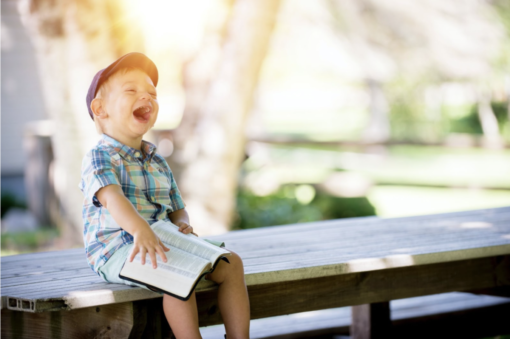 Enfant assis sur un banc avec un livre ouvre la bouche de joie