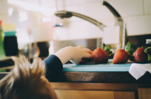 Un très jeune enfant ramasse une fraise sur un plan de travail de cuisine