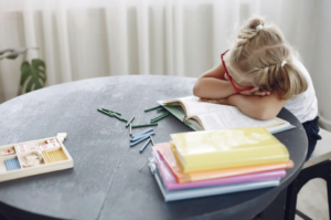 jeune fille assise à une table de travail avec la tête posée dans ses bras