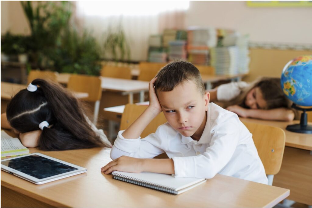 enfant en classe devant son bureau qui s'ennuie
