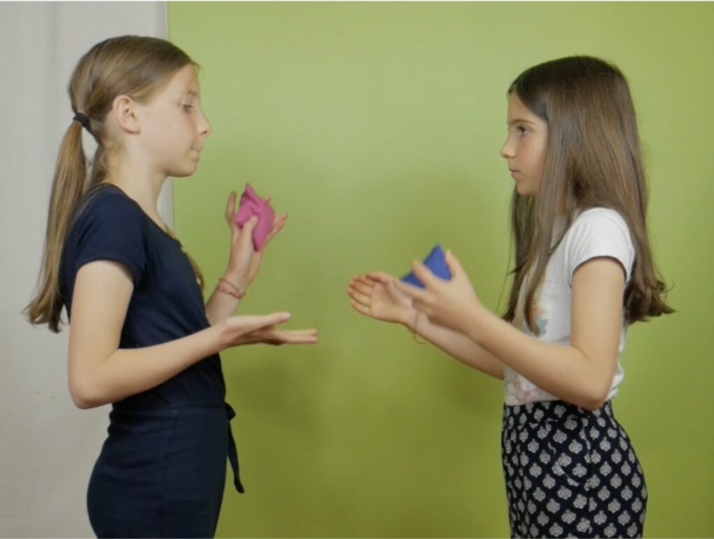 deux filles face à face jouent à se passer un petit coussin de sable