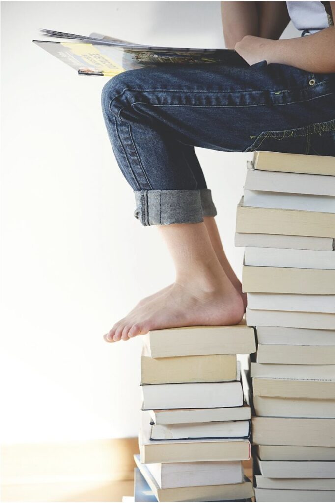 enfant assis sur une pile de livre en train de lire une bande dessinée