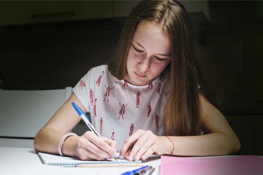 jeune fille en train d'écrire dans un cahier avec un stylo