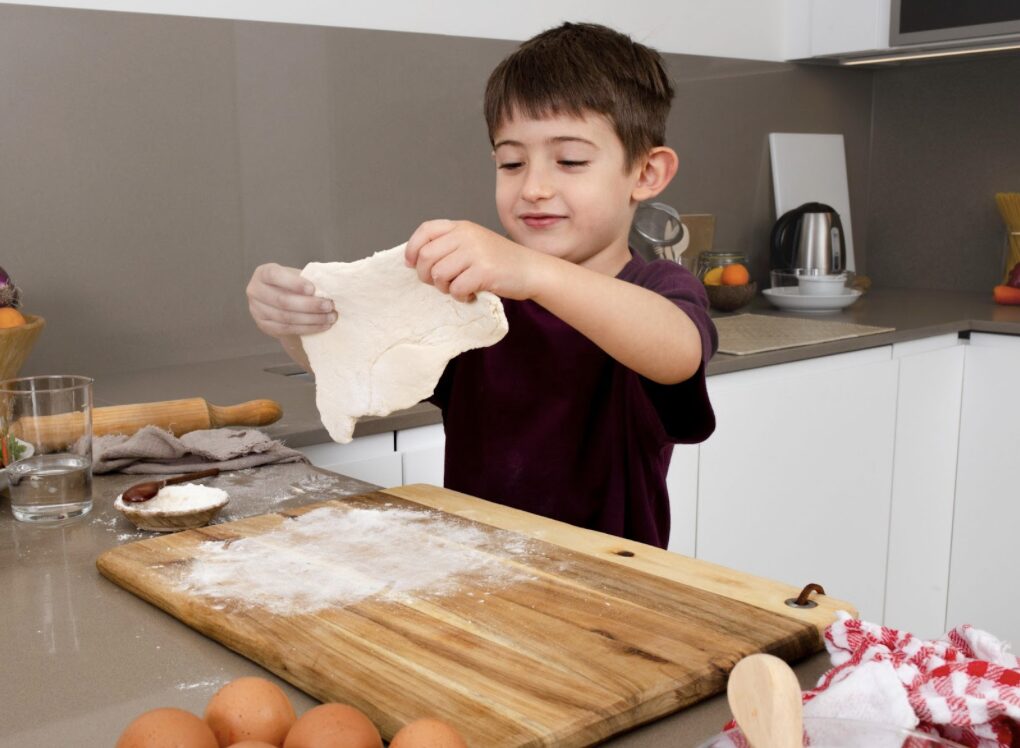 jeune garçon en train d'étaler de la pâte à pizza