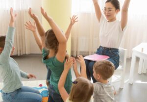 enseignant qui chante une comptine avec des gestes à plusieurs enfants