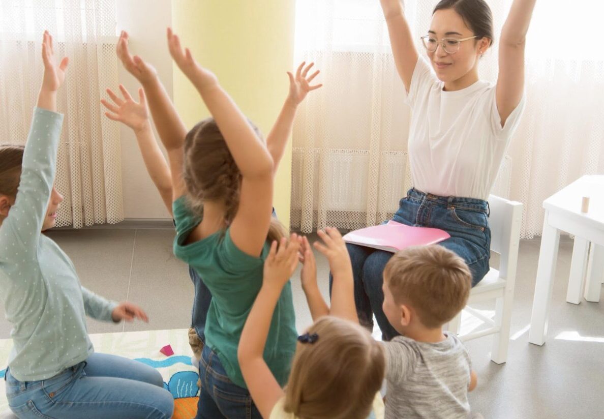 enseignant qui chante une comptine avec des gestes à plusieurs enfants