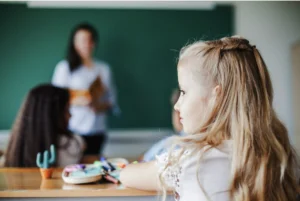 Jeune fille en classe vue de dos en train de regarder par la fenêtre pendant que l'enseignante parle