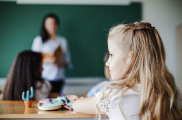 Jeune fille en classe vue de dos en train de regarder par la fenêtre pendant que l'enseignante parle