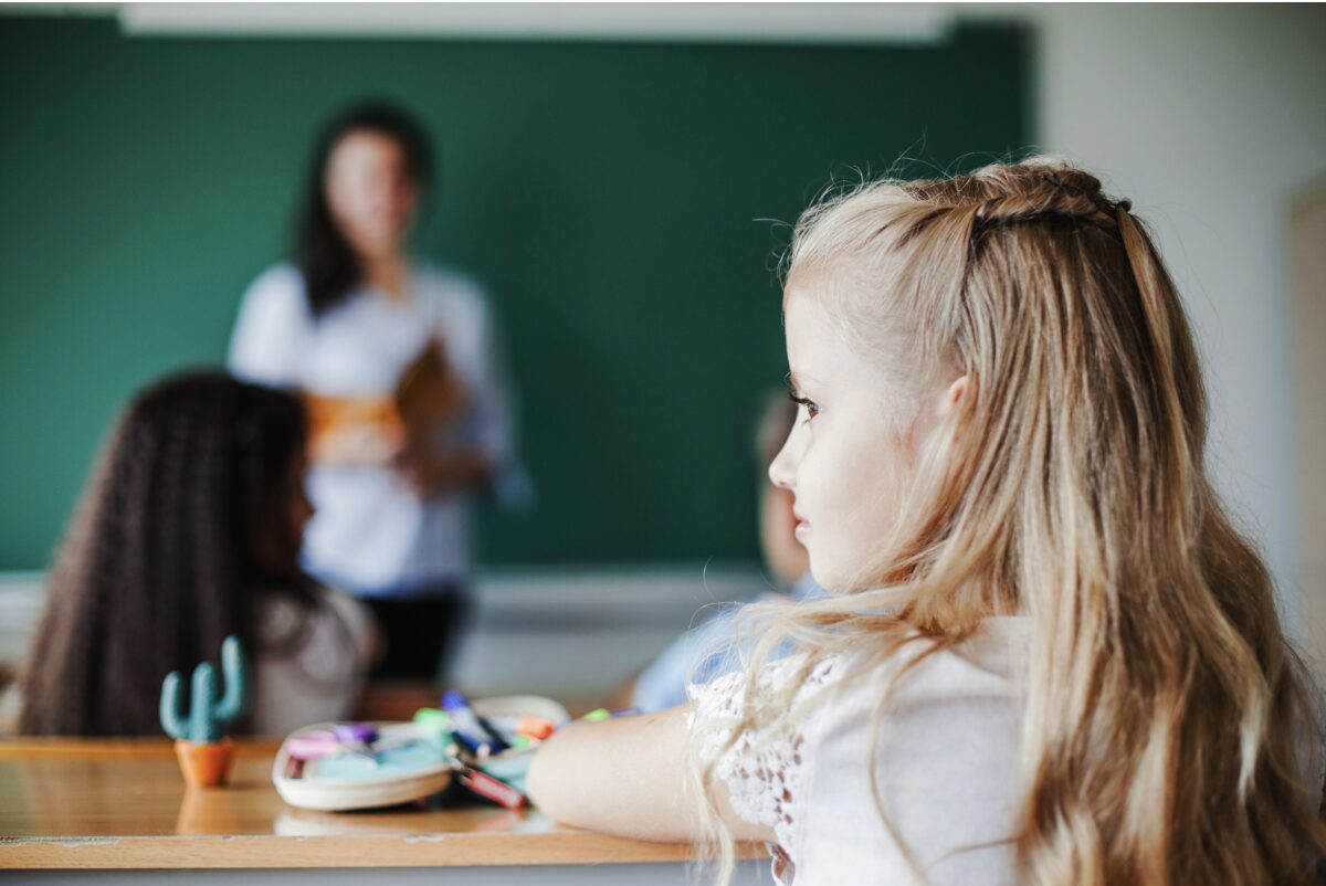 Jeune fille en classe vue de dos en train de regarder par la fenêtre pendant que l'enseignante parle