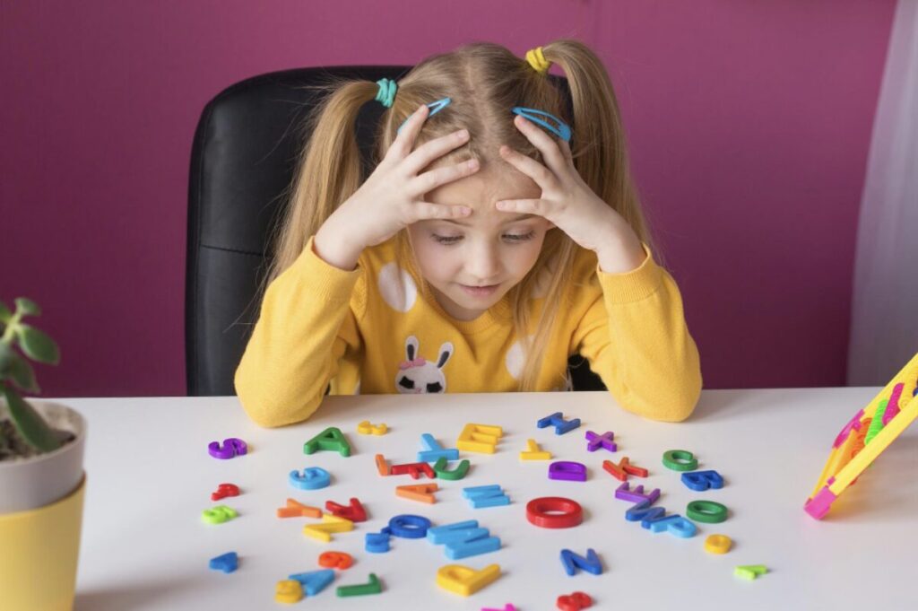 Jeune fille en train de regarder plein de lettres en plastiques disposées devant elle sur une table. Une pratique à éviter avec des enfants qui ne sont pas prêts à entrer dans la lecture