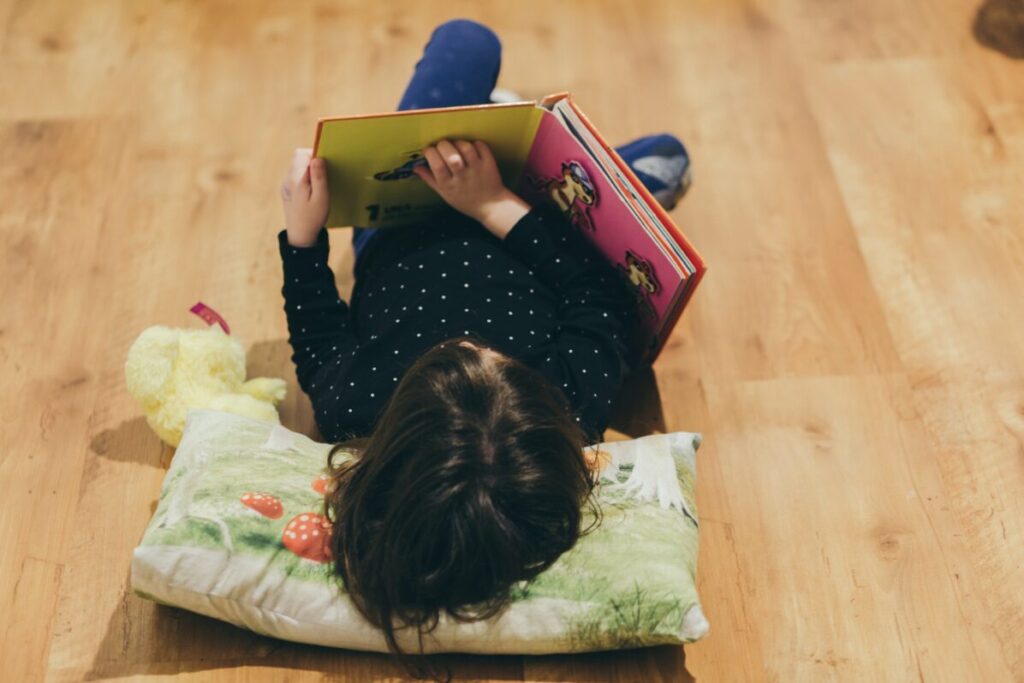 Enfant allongé au sol, la tête sur un oreiller, en train de lire un livre d'histoire