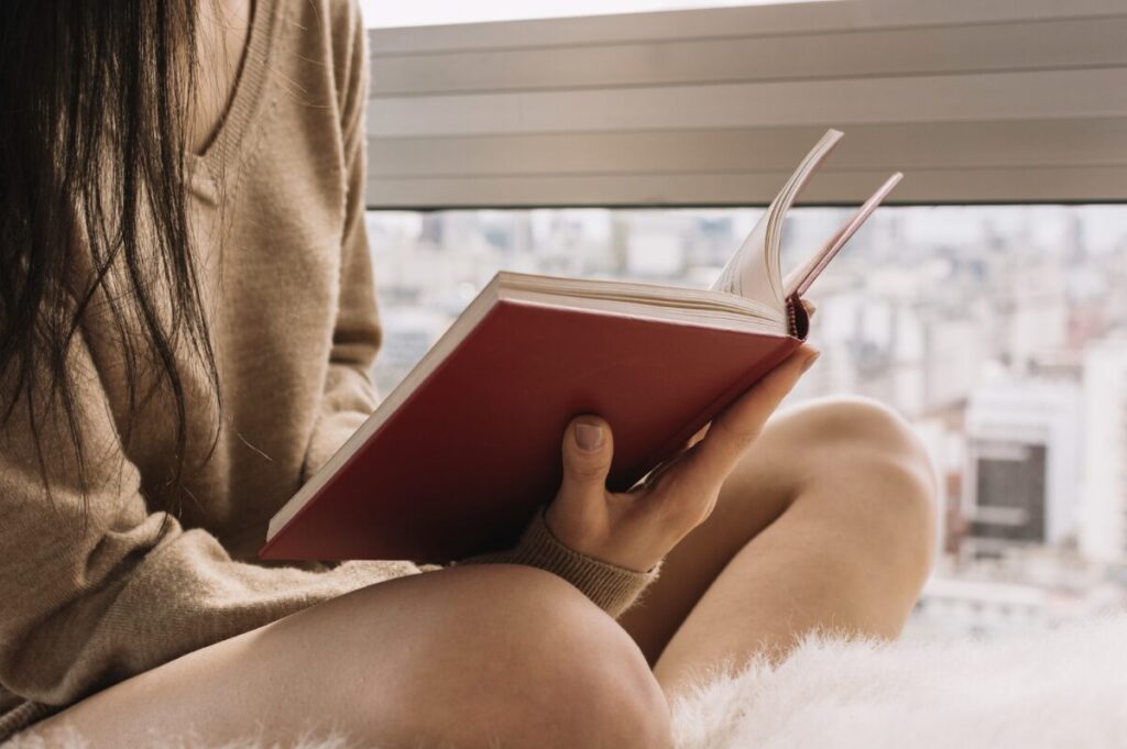Personne assise en tailleur en train de lire un livre rouge