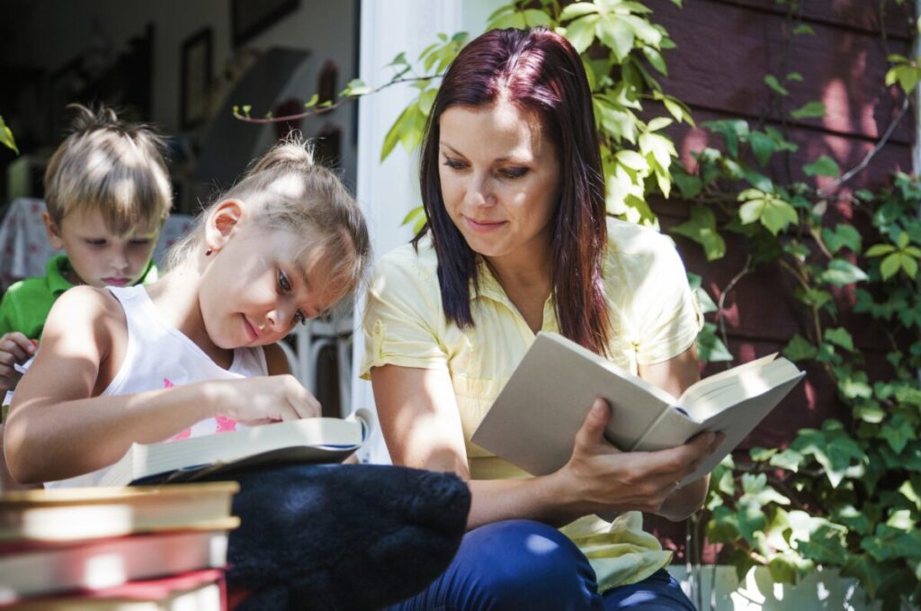 Maman en train de lire un livre dans un espace nature avec sa fille qui lit à côté d'elle