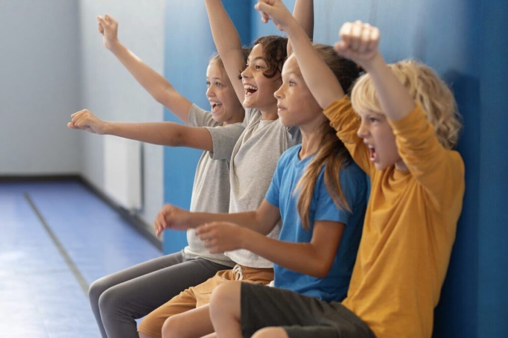 Groupe d'enfants assis sur un banc dans une école en train de lever les bras de joie