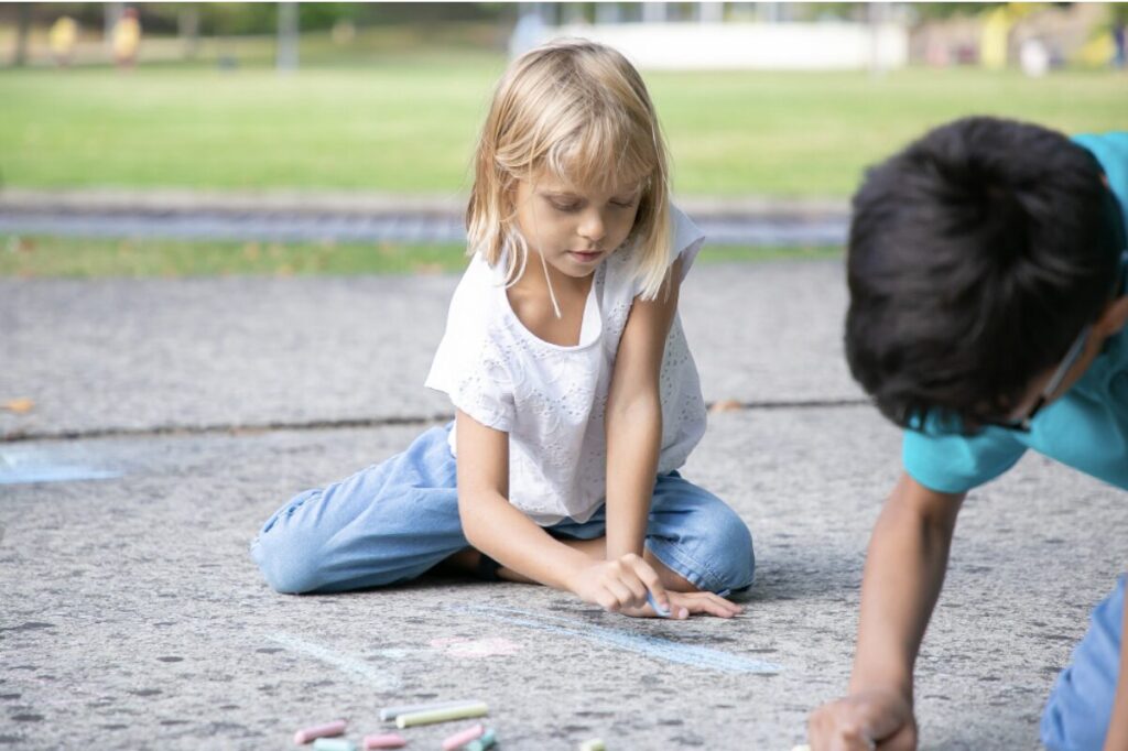 Enfants en train de dessiner au sol avec des craies