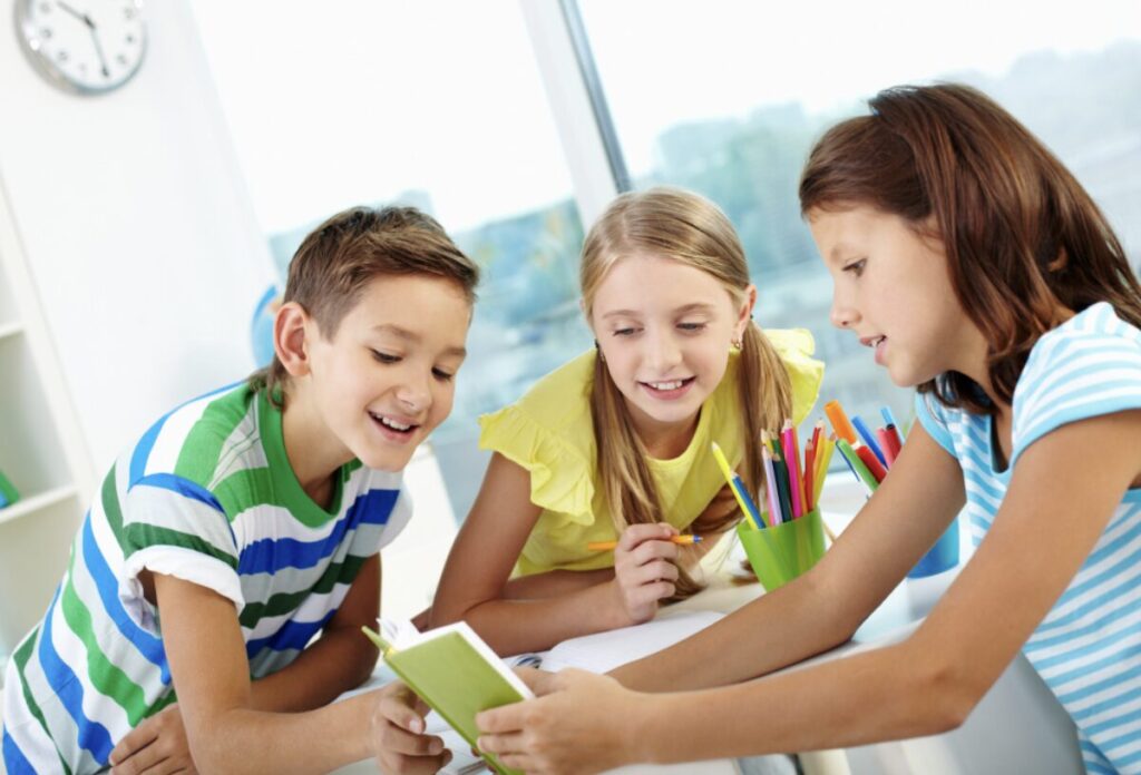 trois enfants en train de regarder avec joie un livre pour apprendre la grammaire