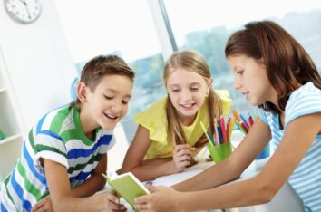 trois enfants en train de regarder avec joie un livre pour apprendre la grammaire