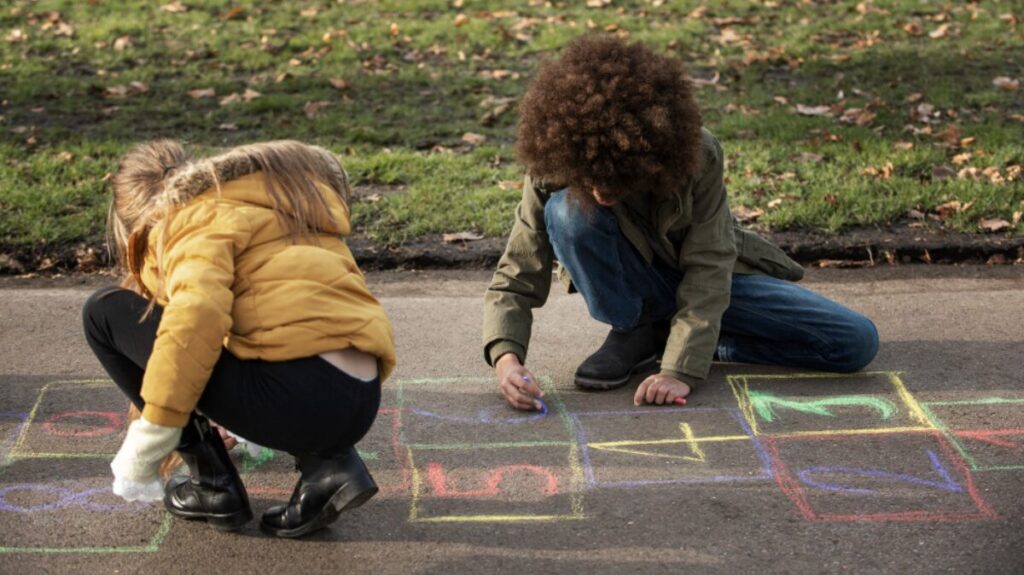 Deux enfants en train de jouer dehors, avec des craies pour dessiner des dessins au sol