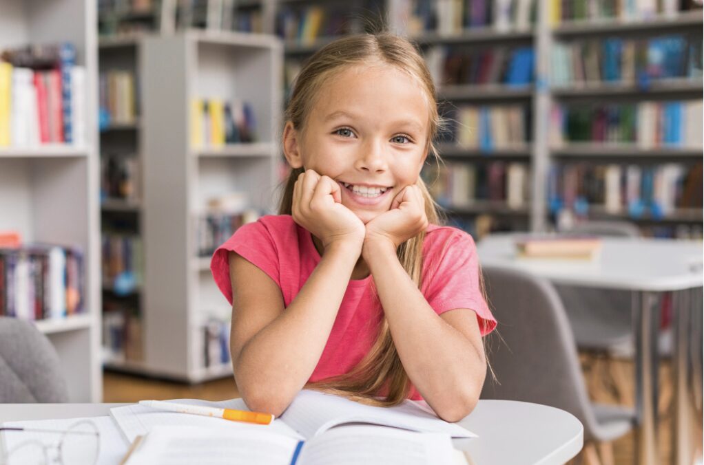 Jeune fille assise à son bureau d'école avec un grand sourire pour montrer sa joie d'apprendre et de réussir