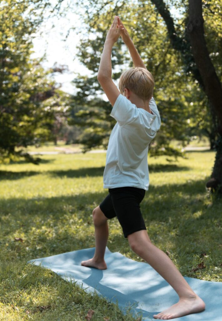 Garçon dans un espace végétalisé, debout sur une serviette, en train de faire un mouvement physique conscient et lent pour retrouver son potentiel d'apprentissage