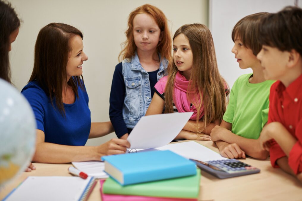 groupe d'enfants rassemblés autour de l'enseignant en train de les encourager pour leur réussite à l'école