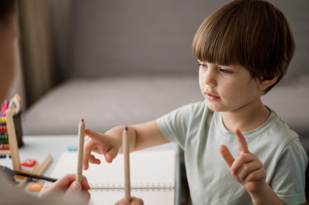 Jeune garçon en train de montrer avec le doigt un crayon de couleur pour travailler sa connaissance des couleurs et progresser dans ses apprentissages