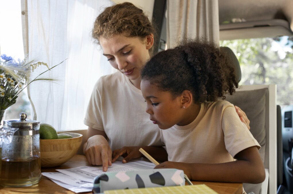 Jeune fille en train de faire ses devoirs avec sa mère qui pointe du doigt une erreur d'orthographe